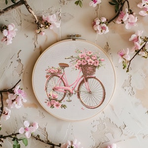 Puede incluir: Una bicicleta rosa con una cesta llena de flores rosas, bordada en un lienzo blanco, enmarcada en un aro de madera.
