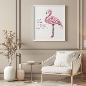 May include: A framed print featuring a pink flamingo illustration. The flamingo is adorned with floral details and stands on one leg. Text on the left reads "Look on the pink side of life". The artwork is displayed in a white frame.