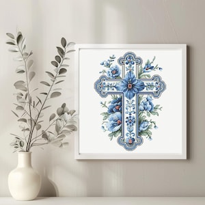 May include: A framed cross-stitch artwork featuring a blue floral cross design. The cross is adorned with blue flowers and foliage, set against a white background. The artwork is framed in a white square frame.