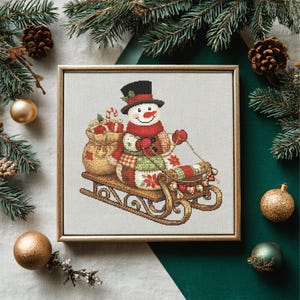 Puede incluir: Imagen de punto de cruz de un muñeco de nieve en un trineo de madera, con sombrero de copa, bufanda y guantes. El muñeco de nieve está rodeado de decoraciones navideñas, incluyendo ramas de pino, bolas y piñas. Una bolsa de regalos está detrás del muñeco de nieve.