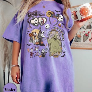 Op de afbeelding: Violetkleurig T-shirt met een grafisch ontwerp met personages uit "The Nightmare Before Christmas". Het ontwerp bevat Jack Skellington, Sally, Oogie Boogie en andere elementen uit de film. Het shirt heeft een comfortabele, oversized pasvorm.