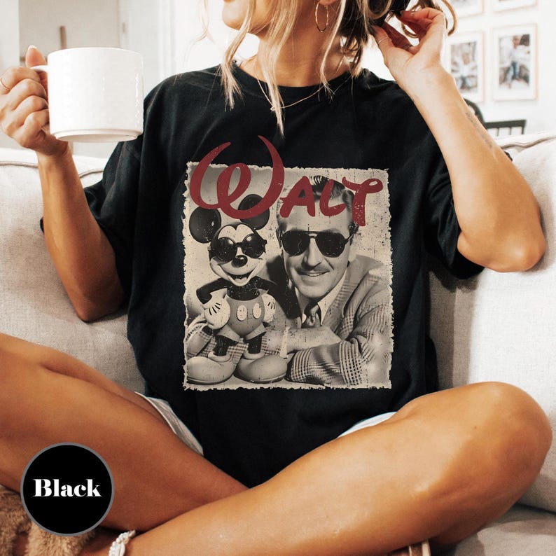 May include: Black t-shirt featuring a vintage graphic of Mickey Mouse wearing sunglasses next to a sepia-toned image of Walt Disney. The word "WALT" is printed in red above the images. The shirt is a relaxed fit.