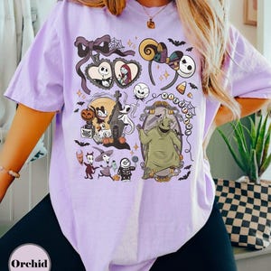 Op de afbeelding: Een lichtpaars T-shirt met een grafisch ontwerp met personages en elementen uit "The Nightmare Before Christmas". Het ontwerp bevat Jack Skellington, Sally, Oogie Boogie en andere iconische beelden. Het shirt heeft een relaxte pasvorm.