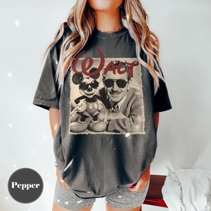 May include: Dark gray t-shirt featuring a vintage-style graphic of Mickey Mouse wearing sunglasses next to Walt Disney, with the word "WALT" in red above. The shirt has a relaxed fit and short sleeves.