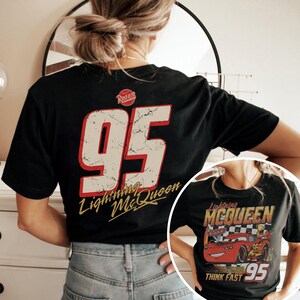 May include: Black t-shirt featuring a distressed design with the number 95 in white and red, and the words "Lightning McQueen" in gold script. A smaller image of Lightning McQueen is visible on the front of the shirt.