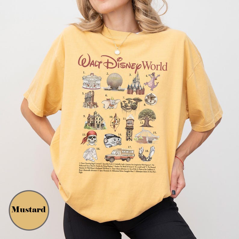 May include: Mustard-coloured t-shirt with a graphic of Walt Disney World icons. The shirt displays illustrations of the park's landmarks, including Cinderella's Castle, Spaceship Earth, and the Hollywood Tower Hotel. The text "Walt Disney World" is printed at the top.