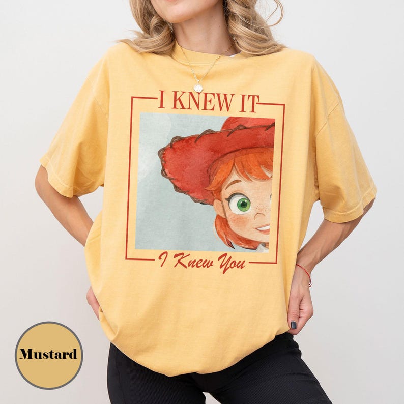 K&ouml;nnte beinhalten: Ein senfgelbes Kurzarm-T-Shirt mit einem Grafikdruck einer Zeichentrickfigur mit roten Haaren und einem roten Hut. Der Text "I KNEW IT" steht &uuml;ber der Grafik und "I Knew You" darunter, alles in einem roten quadratischen Rahmen eingefasst.