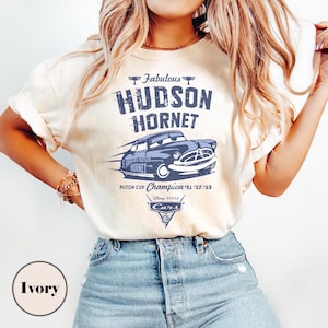 Puede incluir: Camiseta color marfil con un gr&aacute;fico azul del coche de carreras Hudson Hornet, texto "Fabulous Hudson Hornet" y "Piston Cup Champion '51 '52 '53". Incluye el logotipo de Disney Pixar Cars.
