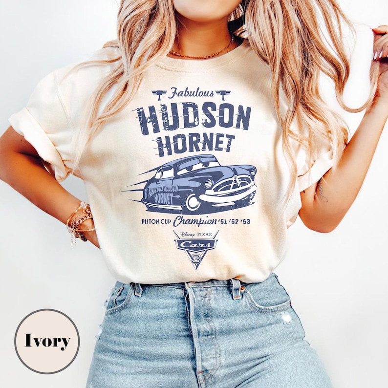 Puede incluir: Camiseta color marfil con un gr&aacute;fico azul del coche de carreras Hudson Hornet, texto "Fabulous Hudson Hornet" y "Piston Cup Champion '51 '52 '53". Incluye el logotipo de Disney Pixar Cars.