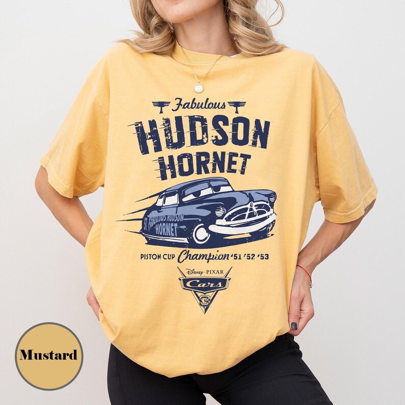 Puede incluir: Camiseta de color mostaza con un gr&aacute;fico del coche de carreras Hudson Hornet de la pel&iacute;cula Cars de Disney Pixar. El dise&ntilde;o incluye el texto "Fabulous Hudson Hornet" y "Piston Cup Champion '51 '52 '53".