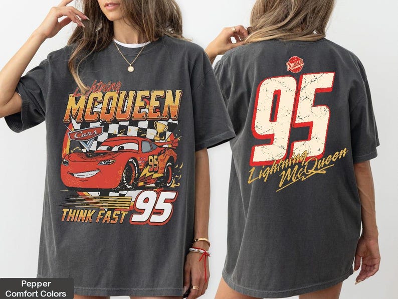 May include: Dark grey t-shirt featuring a graphic of Lightning McQueen from the Cars movie. The front design includes the text "Lightning McQueen Cars 95 Think Fast". The back of the shirt displays the number "95" and "Lightning McQueen".