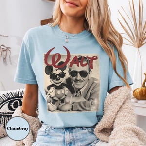 May include: Light blue t-shirt featuring a vintage graphic of Mickey Mouse and Walt Disney wearing sunglasses, with the word "Walt" in red script. The shirt is a soft, comfortable material.