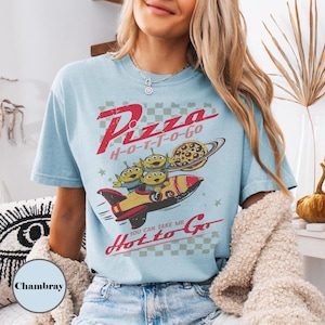 May include: Pale blue t-shirt with a retro graphic. The design includes the text "Pizza H-O-T-T-O-Go", a rocket ship, three green aliens, and a pizza-shaped planet. The shirt has a vintage aesthetic.