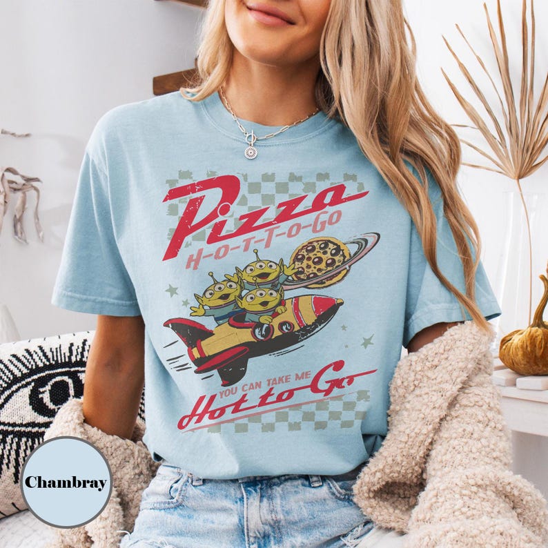 May include: Pale blue t-shirt with a retro graphic. The design includes the text "Pizza H-O-T-T-O-Go", a rocket ship, three green aliens, and a pizza-shaped planet. The shirt has a vintage aesthetic.