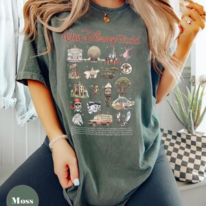 May include: Moss green t-shirt featuring a graphic of Walt Disney World icons. The shirt displays illustrations of various attractions and characters, with the text "Walt Disney World" in red script. A fun and colourful design.