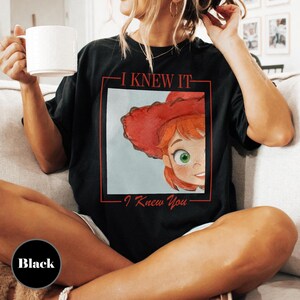 K&ouml;nnte beinhalten: Ein schwarzes T-Shirt mit einem Grafikdruck einer Zeichentrickfigur mit roten Haaren und einem roten Cowboyhut in einem roten quadratischen Rahmen. Der Text "I KNEW IT" steht &uuml;ber dem Rahmen und "I Knew You" steht darunter in roter Schrift.