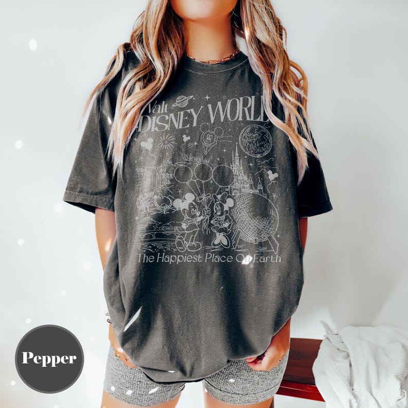 Pu&ograve; includere: T-shirt grigio scuro con una grafica bianca di Topolino e Minnie, palloncini, fuochi d'artificio e un castello. Il testo "Walt Disney World" e "The Happiest Place On Earth" &egrave; anch'esso visualizzato sulla maglietta.