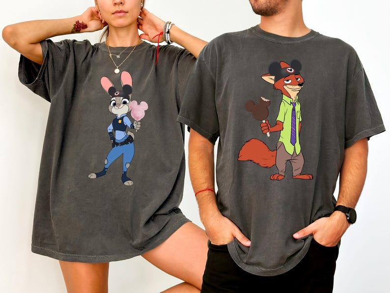 Puede incluir: Dos camisetas gris carb&oacute;n con personajes de dibujos animados. Una camiseta muestra a Judy Hopps sosteniendo algod&oacute;n de az&uacute;car, la otra a Nick Wilde con un helado de Mickey Mouse. Ambas camisetas tienen un aspecto vintage.