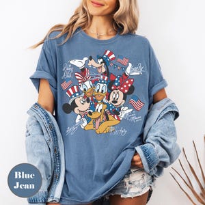 Peut inclure: T-shirt bleu jean avec un motif de personnages Disney Mickey Mouse, Minnie Mouse, Donald Duck, Daisy Duck, Dingo et Pluto, tous v&ecirc;tus de tenues patriotiques. Le t-shirt porte les inscriptions "Mickey Mouse", "Minnie Mouse 2020" et les noms des personnages.