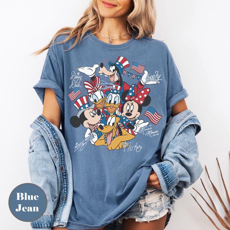 Peut inclure: T-shirt bleu jean avec un motif de personnages Disney Mickey Mouse, Minnie Mouse, Donald Duck, Daisy Duck, Dingo et Pluto, tous v&ecirc;tus de tenues patriotiques. Le t-shirt porte les inscriptions "Mickey Mouse", "Minnie Mouse 2020" et les noms des personnages.