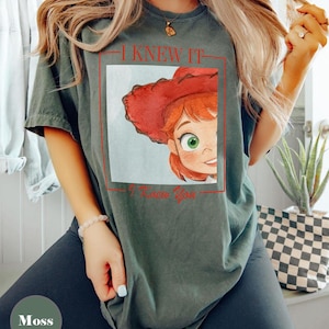 K&ouml;nnte beinhalten: Ein moosgr&uuml;nes Kurzarm-T-Shirt mit einem Grafikdruck einer Zeichentrickfigur mit roten Haaren und einem roten Cowboyhut. Das Design ist in einem roten rechteckigen Rahmen eingefasst, mit dem Text I KNEW IT dar&uuml;ber und I Knew You darunter.