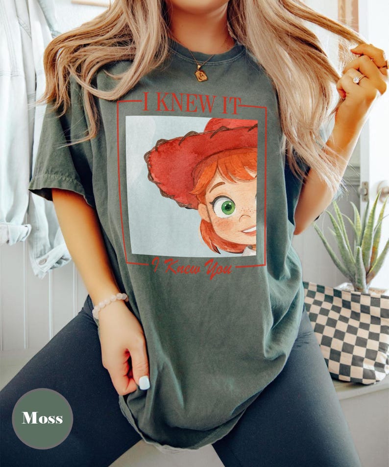 K&ouml;nnte beinhalten: Ein moosgr&uuml;nes Kurzarm-T-Shirt mit einem Grafikdruck einer Zeichentrickfigur mit roten Haaren und einem roten Cowboyhut. Das Design ist in einem roten rechteckigen Rahmen eingefasst, mit dem Text I KNEW IT dar&uuml;ber und I Knew You darunter.