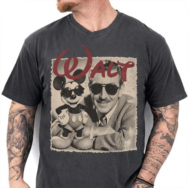 May include: Dark gray v-neck t-shirt featuring a sepia-toned graphic of Walt Disney and Mickey Mouse wearing sunglasses. The word "Walt" is in red script above the image. The shirt is a vintage style.