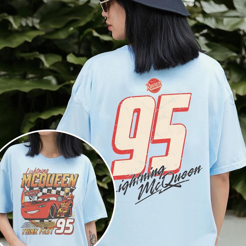 May include: Light blue t-shirt featuring Lightning McQueen graphics. The front displays the character with text, while the back showcases a large "95" and "Lightning McQueen" text. The shirt has a vintage, distressed design.