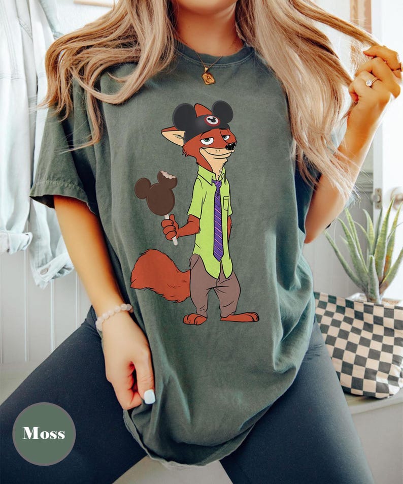 Puede incluir: Camiseta verde musgo con un personaje de zorro de dibujos animados que lleva un sombrero de Mickey Mouse y sostiene un helado con forma de Mickey Mouse. El zorro viste una camisa verde y una corbata morada. La camiseta es de corte holgado.