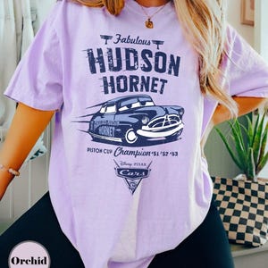 Puede incluir: Camiseta lila claro con un gr&aacute;fico del coche de carreras Hudson Hornet de la pel&iacute;cula Cars de Disney Pixar. El dise&ntilde;o incluye el texto "Fabulous Hudson Hornet" y "Piston Cup Champion '51 '52 '53".