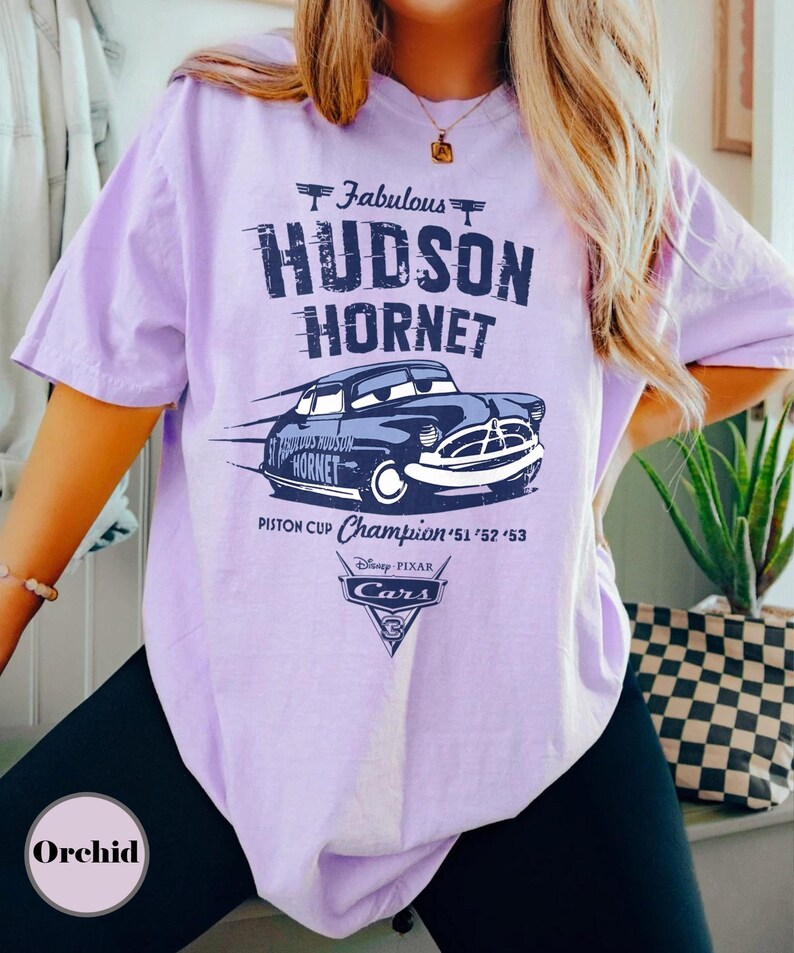 Puede incluir: Camiseta lila claro con un gr&aacute;fico del coche de carreras Hudson Hornet de la pel&iacute;cula Cars de Disney Pixar. El dise&ntilde;o incluye el texto "Fabulous Hudson Hornet" y "Piston Cup Champion '51 '52 '53".