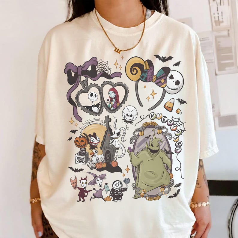 Op de afbeelding: Cr&egrave;mekleurig T-shirt met een ontwerp met personages en elementen uit "The Nightmare Before Christmas". Het ontwerp bevat Jack Skellington, Sally, Zero, Oogie Boogie en andere iconische beelden. Vleermuizen, spinnenwebben en snoepma&iuml;s zijn ook aanwezig.