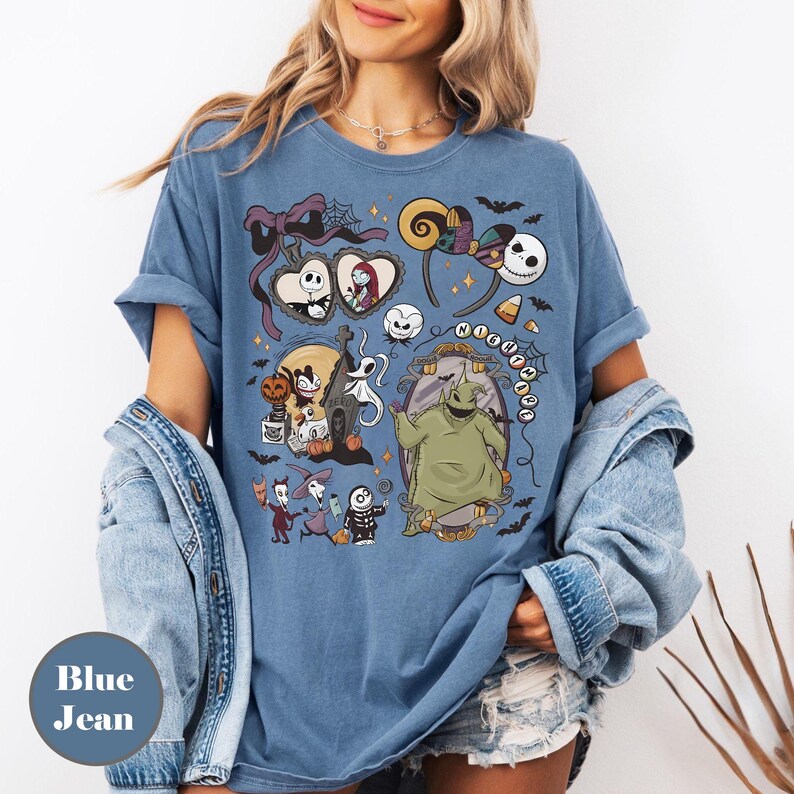 Op de afbeelding: Blauw spijker-T-shirt met een kleurrijke afbeelding van personages uit "The Nightmare Before Christmas". Het ontwerp bevat Jack Skellington, Sally, Oogie Boogie en andere griezelige elementen. Het shirt heeft een ronde hals en korte mouwen.