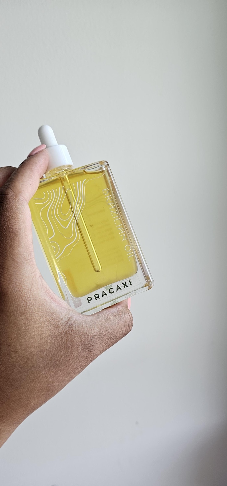 May include: A clear rectangular bottle of Brazilian Pracaxi oil with a white dropper. The bottle contains a yellow liquid and has white text that reads "BRAZILIAN OIL" and "PRACAXI".