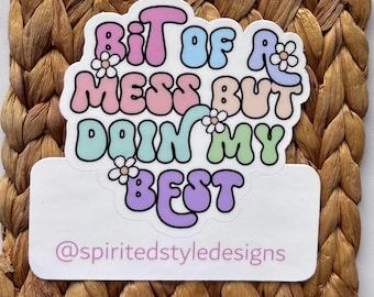May include: A sticker with the text "Bit of a Mess But Doin' My Best" in pastel colors, with daisy accents. The sticker also includes the Instagram handle "@spiritedstyledesigns" on a white rectangle.