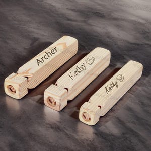 May include: Three wooden whistles with names engraved on them. The first whistle says "Archer", the second says "Kathy" with a cat icon, and the third says "Kathy" with a dog icon.