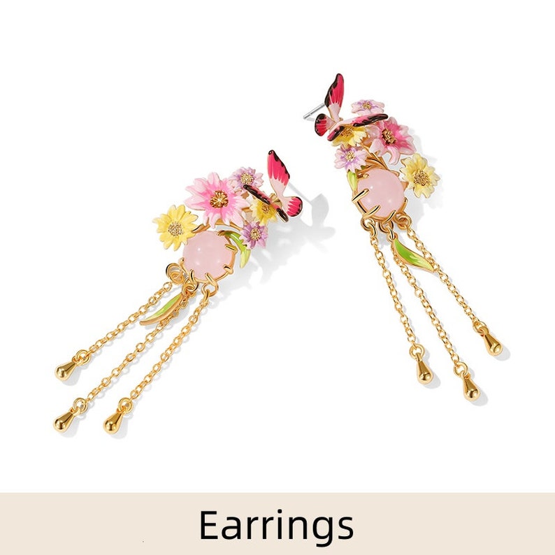 May include: A pair of gold earrings with pink and yellow flower accents, butterflies, and dangling chains. The earrings feature a pink stone in the center of each flower cluster.