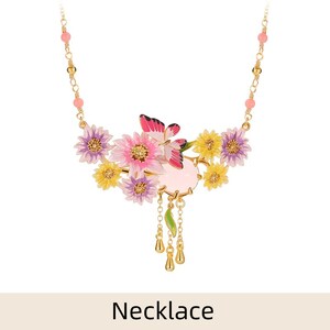 May include: A delicate gold necklace with a pink and yellow floral design. The pendant features a pink butterfly, pink and yellow flowers, and a pink stone. The necklace has a chain with small pink beads.