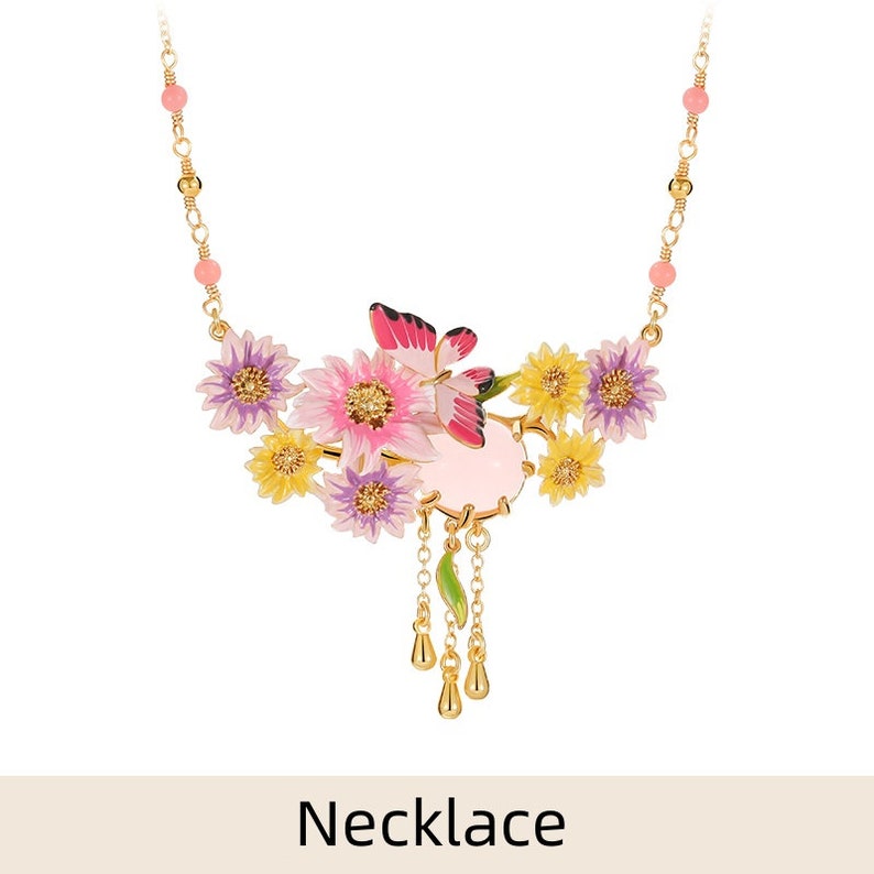 May include: A delicate gold necklace with a pink and yellow floral design. The pendant features a pink butterfly, pink and yellow flowers, and a pink stone. The necklace has a chain with small pink beads.