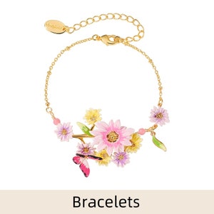 May include: A gold chain bracelet with a floral design featuring pink, yellow, and purple flowers and a pink butterfly charm. The bracelet is part of a collection of bracelets.