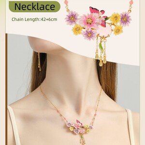 May include: A gold necklace with a pink, yellow, and purple flower pendant. The pendant features a butterfly and a pink stone. The chain is 42 inches long with a 6-inch extender.