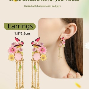 May include: A pair of gold dangle earrings with pink and yellow flowers, butterflies, and green leaves. The earrings are 1.8 inches by 6.5 inches.