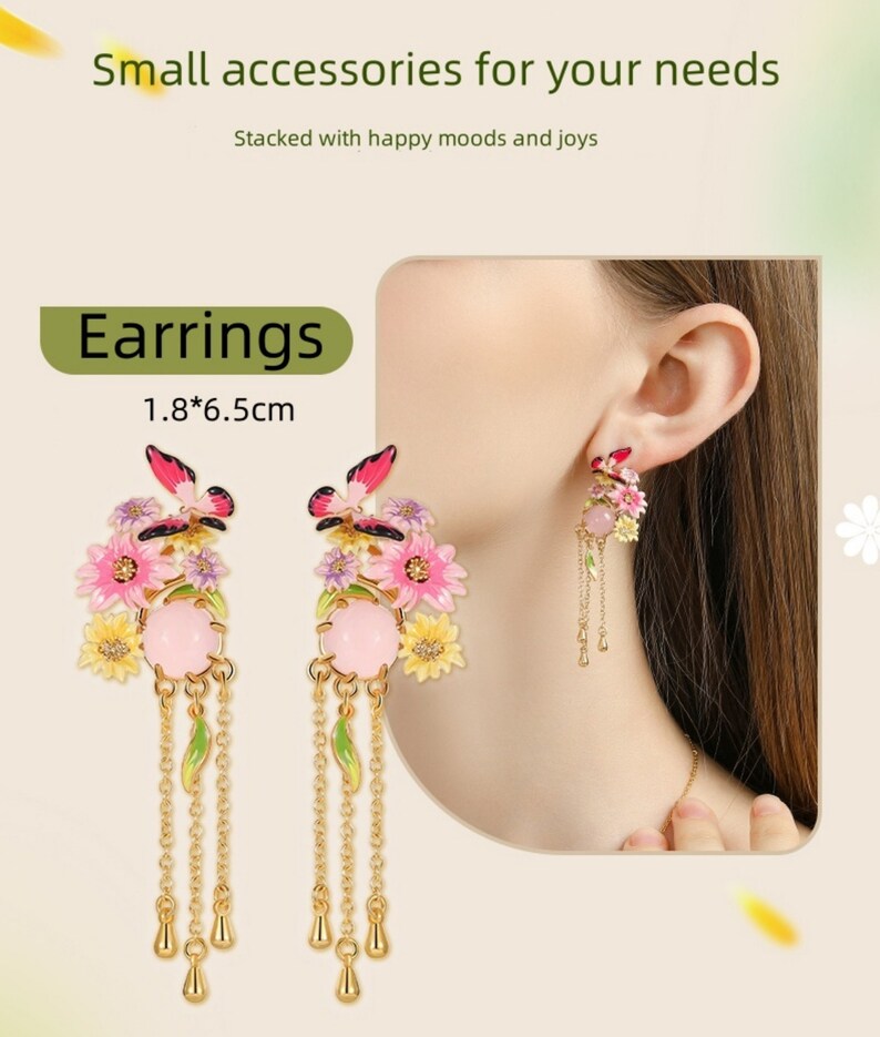 May include: A pair of gold dangle earrings with pink and yellow flowers, butterflies, and green leaves. The earrings are 1.8 inches by 6.5 inches.