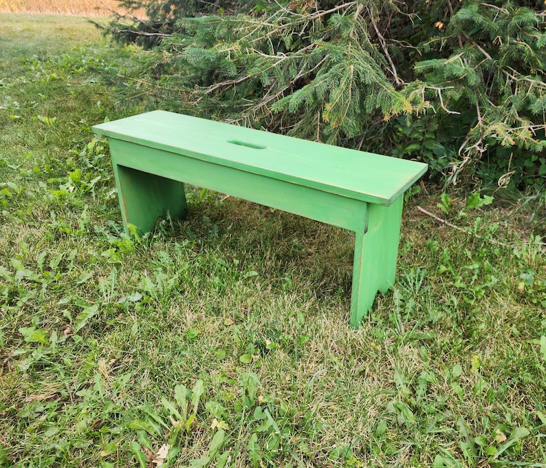 May include: A green wooden bench with a simple design. The bench is made of solid wood and has a natural finish. It is perfect for adding a touch of rustic charm to any outdoor space.