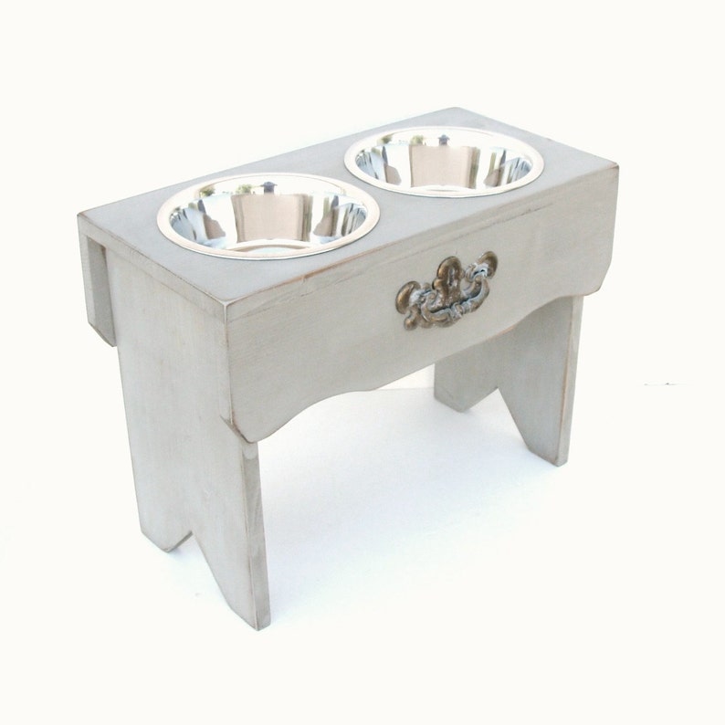 Puede incluir: Un soporte elevado para cuencos de perro de madera gris con dos cuencos de acero inoxidable y un tirador de caj&oacute;n decorativo.