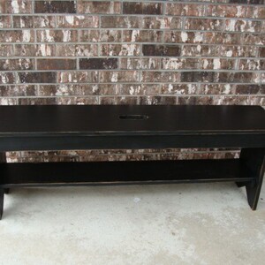 May include: A black wooden bench with a shelf underneath. The bench has a distressed finish and a small cutout in the top.