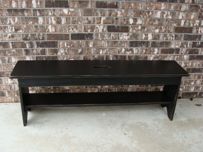 May include: A black wooden bench with a shelf underneath. The bench has a distressed finish and a small cutout in the top.