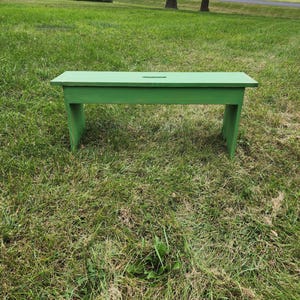 May include: A green wooden bench with a simple design, sitting on a grassy lawn.