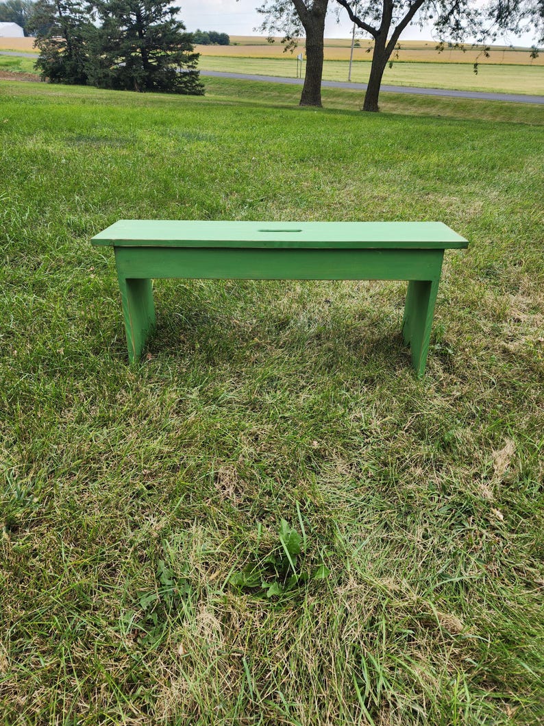 May include: A green wooden bench with a simple design, sitting on a grassy lawn.