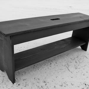 Pu&ograve; includere: Una panca in legno nero con uno scaffale. La panca ha un piano rettangolare con un piccolo foro al centro. Lo scaffale &egrave; sotto il piano ed &egrave; anch'esso in legno.